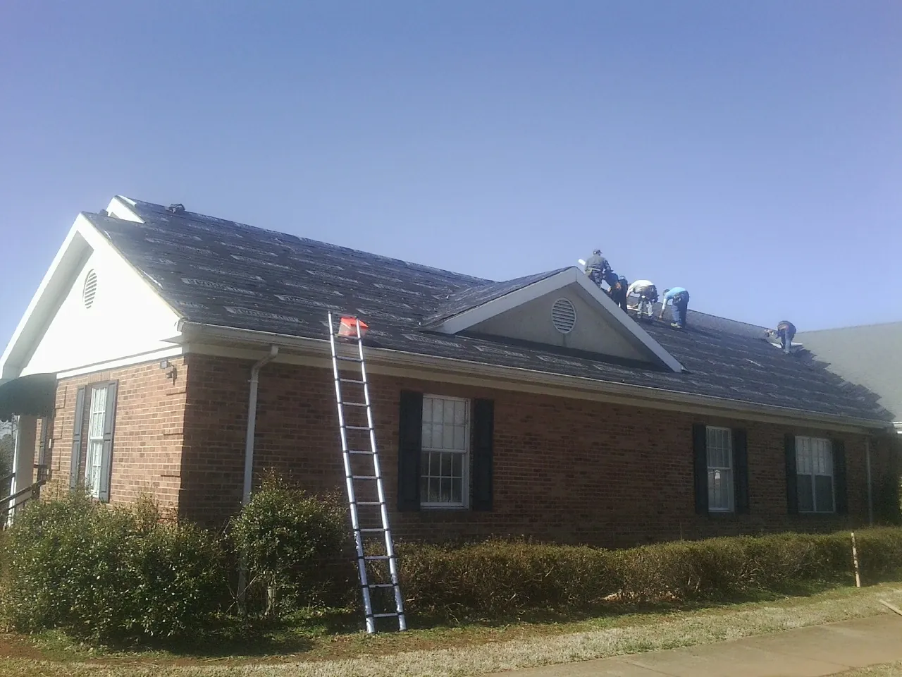 Crew tearing shingles off a brick ranch roof with a ladder set — Emergency Roof Repair work by our crew in Wind Gap