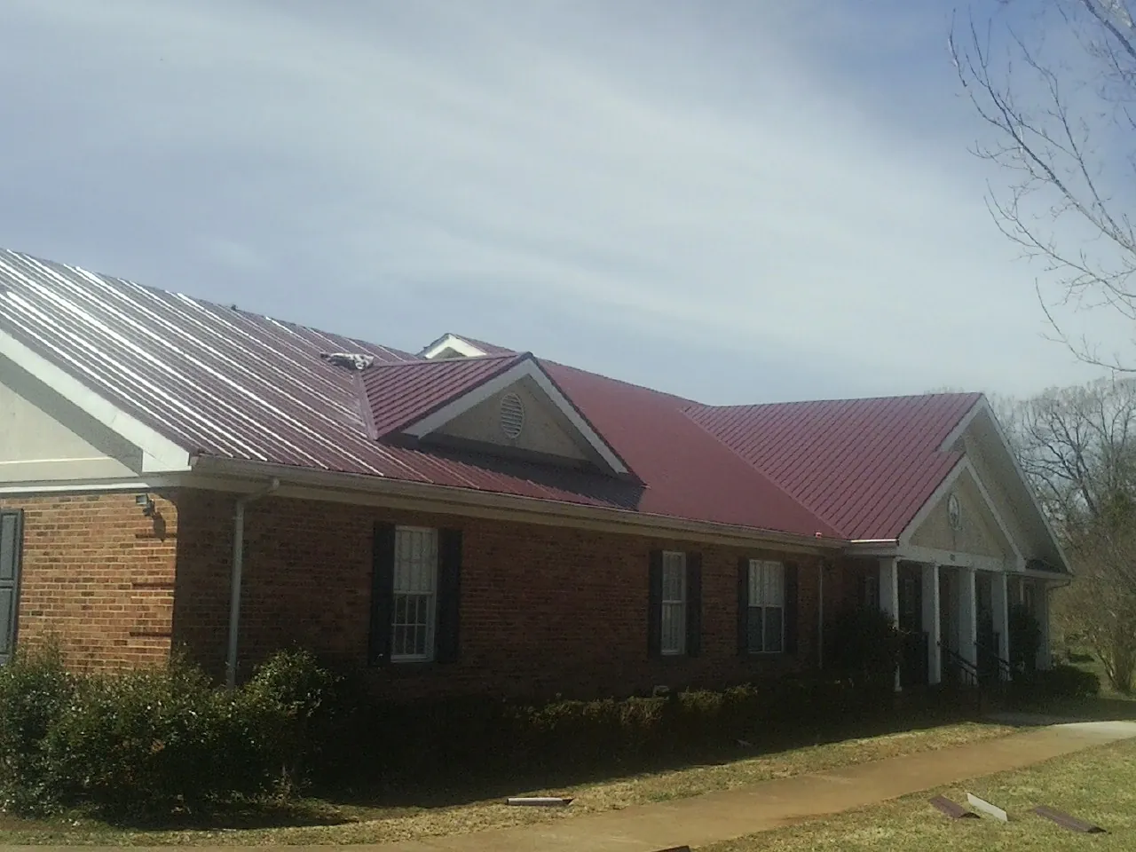 Red metal roof with gabled entries on a long brick building, from a Hail Damage Roof Repair job in Wind Gap