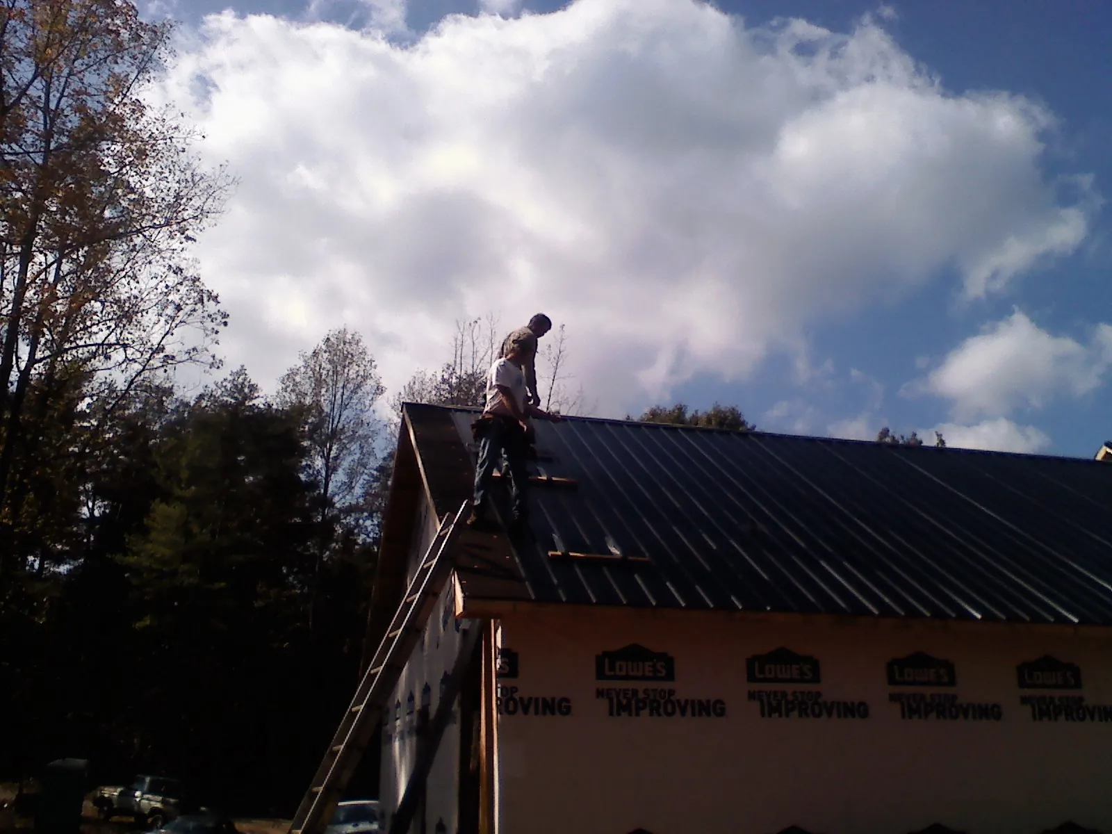 Roofer fastening dark metal panels high against a cloudy sky, from a Roof Inspection job in Wind Gap